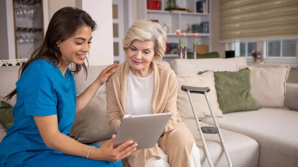 Carer and elderly woman sitting on a sofa looking at a tablet together