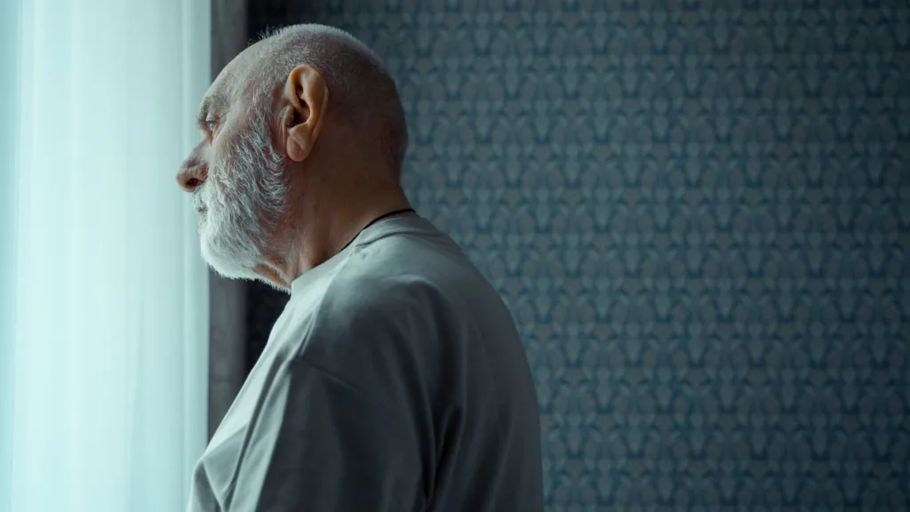 an elderly man alone looking out the window